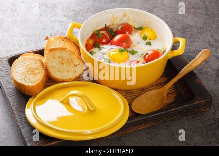 Eier en Cocotte gebacken mit Tomaten, Petersilie, Fleisch, Käse in der Nähe in der Holzschale auf dem Tisch. Horizontal Stockfoto