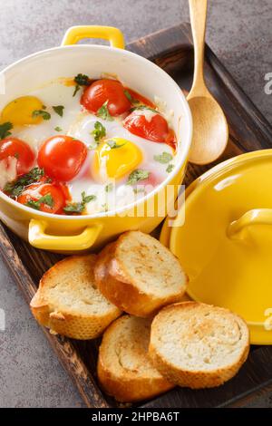 Eierkokotte mit Käse und Gemüse serviert mit frischer Petersilie und Toast in der Nähe in der Holzschale auf dem Tisch. Vertikal Stockfoto