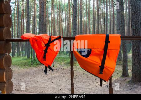 Leuchtend orange Rettungswesten für Kinder und Erwachsene hängen an der Geländer eines Waldhauses. Stockfoto