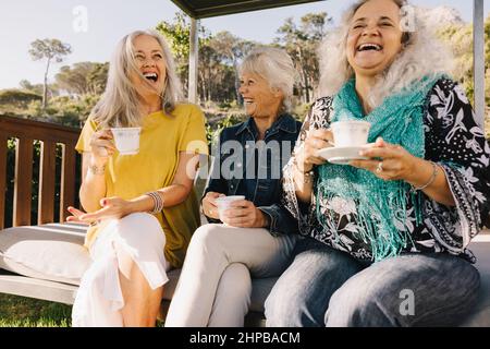 Ältere Frauen lachen glücklich, während sie zusammen Tee trinken. Gruppe älterer Freunde, die ihren Sommerurlaub in einem Spa-Resort genießen. Drei reife Frauen e Stockfoto