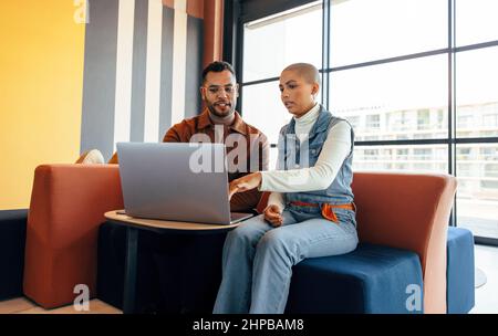 Junge Geschäftsleute, die in einer Bürolobby eine wichtige Diskussion führen. Zwei Kollegen aus dem Unternehmen nutzen einen Laptop in einem modernen Co-Working-Bereich. Zwei junge Stockfoto