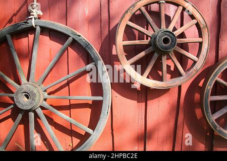 Auswahl an traditionellen Holzrädern in verschiedenen Größen, die an einer roten Holzschuppen-Wand hängen. Stockfoto