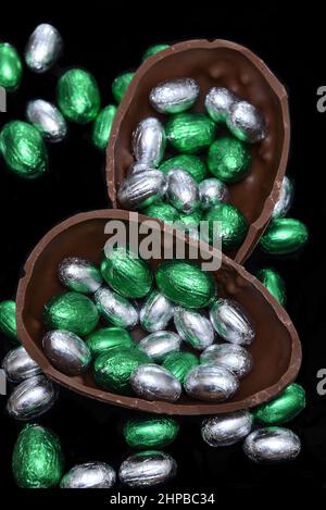 Bunte, in Folie verpackte Schokoladen-ostereier in Silber und Grün mit zwei Hälften eines großen braunen Milchschokoladeneier in der Mitte und Mini-Eiern. Stockfoto