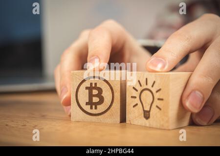 Konzept des Bitcoin-Wachstums. Bulb-Idee und BTC-Symbole auf einem Holzwürfel in der Nahaufnahme der Hände. Foto der Unternehmensinvestition Stockfoto