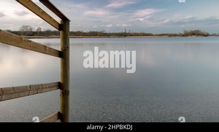 Holzzaun am Ufer eines Sees in der blauen Stunde Stockfoto