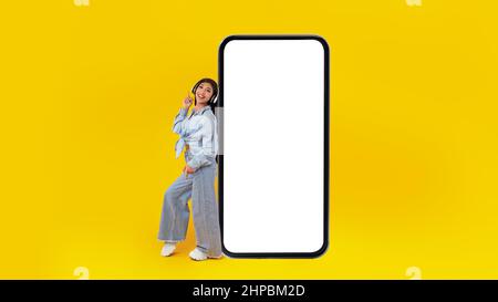 Fröhliche Dame, die sich auf das Mobiltelefon lehnt und Musik hört Stockfoto