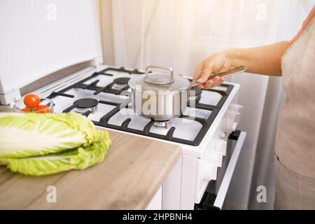 Frau stellt Edelstahl Topf auf Gasherd in der modernen Küche. Kochgeschirr Konzept Stockfoto