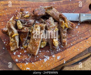 Nahaufnahme von frisch gekochtem Schweinefleisch Secreto de ventresca pure iberico, iberisches Schwein geschnitten, mit Knoblauch, Salzsteinen, Rosmarin und einem Messer auf einem Holzbrett Stockfoto