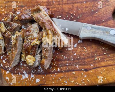 Nahaufnahme von frisch gekochtem Schweinefleisch Secreto de ventresca pure iberico, iberisches Schwein geschnitten, mit Knoblauch, Salzsteinen, Rosmarin und einem Messer auf einem Holzbrett Stockfoto