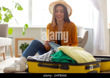 Reisevorbereitung. Fröhliche junge kaukasische Frau, die Koffer packt, sich für den Urlaub zu Hause vorbereitet, Platz kopiert Stockfoto