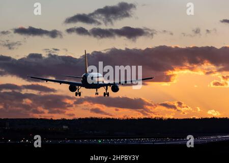 Flugzeuge landen am Flughafen Stuttgart, Fahrwerk nach unten, gegen den goldenen Sonnenuntergangshimmel mit einigen Wolken, teilweise verwischt durch die Hitze der Düsentreibmaschinen Stockfoto