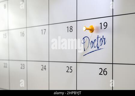 Ärzte Termin Konzept. Ein Kalender mit einem Eintrag „Doctor“ und einem Daumennack. Selektiver Fokus. Stockfoto