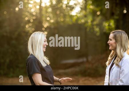 Zwei medizinische Frauen mit schwarzen Peelings und eine trägt einen weißen Laborkittel, der draußen steht und redet Stockfoto