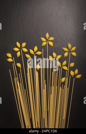 Blumen aus einer Vielzahl von ungekochten Nudeln, isoliert auf dunklem Schieferhintergrund, Diät- und Lebensmittelkonzept, Draufsicht mit Kopierraum Stockfoto