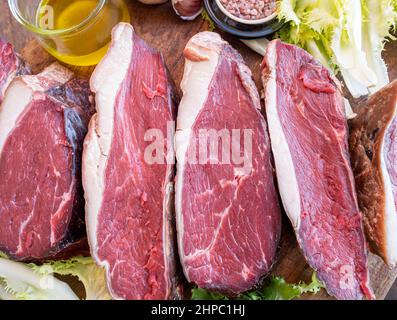 21 Tage trocken gereifte rohe schwarze angus picanha mit Olivenöl, Knoblauch, rosa Salz und Salat auf einem Holzbrett. Stockfoto