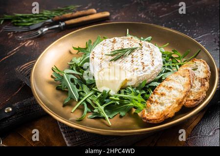 Salat mit gegrilltem Camembert-Käse, Rucola, Toast und Rosmarin auf einem Teller. Dunkler Hintergrund. Draufsicht Stockfoto