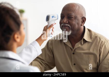 Arzt überprüft die Temperatur des alten Mannes mit einem Infrarot-Thermometer Stockfoto