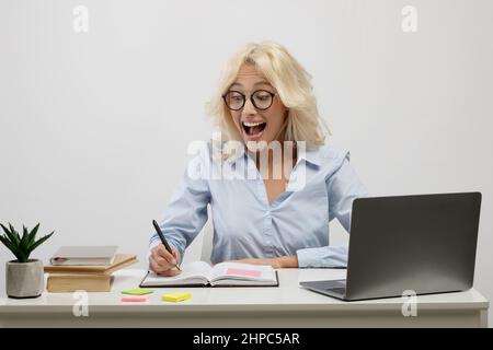 Überraschte eine Geschäftsfrau, die am Laptop arbeitete und sich Notizen in einem Notizbuch machte und überraschend ihre Notizen am Arbeitsplatz las Stockfoto