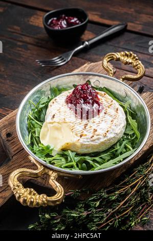 Gebackener Camembert Brie-Käse mit Cranberry-Sauce und garniert mit Rucola-Salat in einer Pfanne. Holzhintergrund. Draufsicht Stockfoto