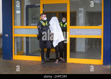 Hamburg, Deutschland. 20th. Februar 2022. Polizisten führen einen Verdächtigen in Handschellen aus dem Haus. Am Sonntag wurde in Hamburg-Niendorf eine Frau mit lebensbedrohlichen Stichverletzungen gefunden. Nach Angaben eines Sprechers hatte ein Bewohner im Flur Blut gesehen und die Notdienste benachrichtigt. Nach ersten Informationen wurde von einer Auseinandersetzung gesprochen, bei der eine Frau mit einem Messer verletzt worden war. Quelle: Jonas Walzberg/dpa/Alamy Live News Stockfoto