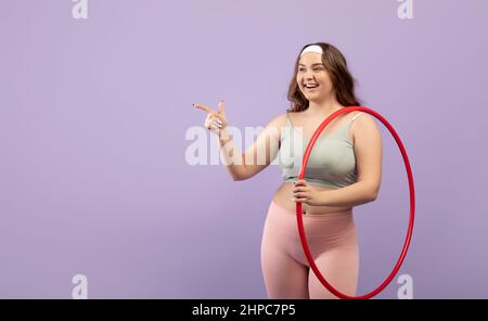 Zufrieden aufgeregt plus Größe europäische junge Frau in Sportbekleidung mit offenem Mund mit Hula Hoop Reifen Stockfoto