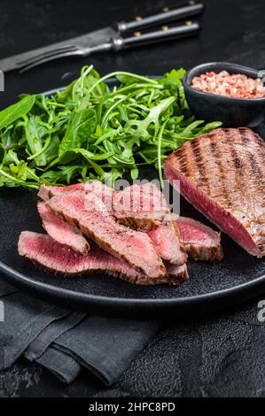 BBQ gegrilltes Rock Steak auf einem Teller mit grünem Salat. Schwarzer Hintergrund. Draufsicht Stockfoto