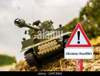 Ukraine Konflikt Warnschild mit Tank im Hintergrund in deutscher Sprache Stockfoto