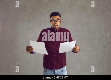 Afroamerikanischer Mann mit einem verwirrten und verwirrten Ausdruck steht mit zwei weißen Blättern Papier. Stockfoto