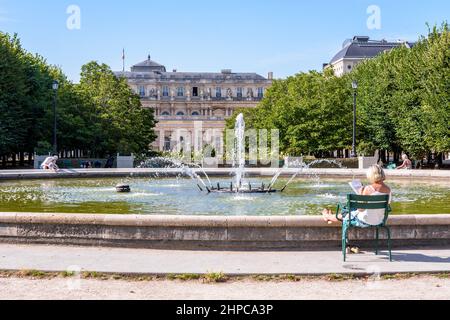 Eine ältere Frau entspannt sich auf einem Metallrasenstuhl am Brunnen im Garten des Palais-Royal in Paris, Frankreich. Stockfoto