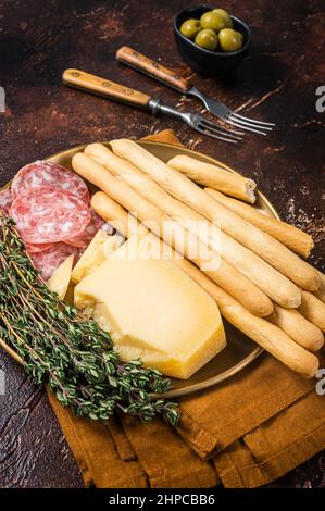 Vorspeiseteller mit Antipasti Snacks, Grissini-Brotscheiben, Salami, Oliven und Parmesankäse. Dunkler Background. Draufsicht Stockfoto