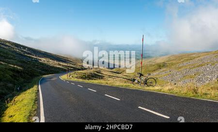 Die berühmte Klettertour auf der Einbahnstraße nach Great Dun Fell im Eden Valley mit dem Fahrrad, das sich gegen den Schneestab in Cumbria, England, gelehnt hat Stockfoto