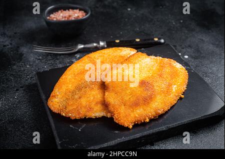 Gebratene panierte Tilapia-Filets auf einem Marmorbrett. Schwarzer Hintergrund. Draufsicht Stockfoto