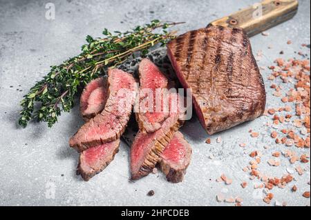 Braten Sie in Scheiben geschnittene Flanke oder Flap Steak auf einem Metzgerspalter mit Thymian und rosafarbenem Salz. Grauer Hintergrund. Draufsicht Stockfoto