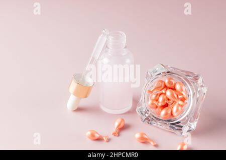 Kosmetikkapseln für das Gesicht aus dem Glas gegossen. Tag und Nacht Gesichts-Serum in Kapseln und Tropfflasche auf rosa Hintergrund. Hautpflege Stockfoto