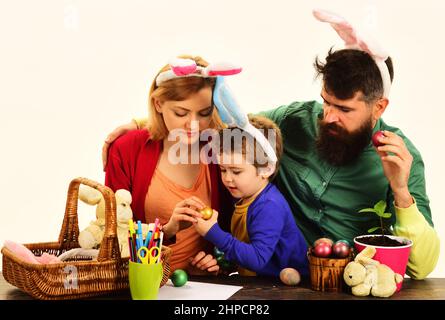 Mutter, Vater und Sohn malen Eier. Glückliche Familie bereitet sich auf Ostern in Hasenohren vor. Stockfoto