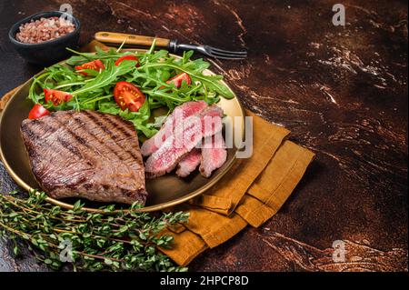 Geröstete Flanke oder Flap Steak auf einem Teller mit Salat. Dunkler Hintergrund. Draufsicht. Speicherplatz kopieren Stockfoto