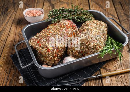 Roher Schweinebauch italienische Porchetta mit Kräutern und Gewürzen. Holzhintergrund. Draufsicht Stockfoto