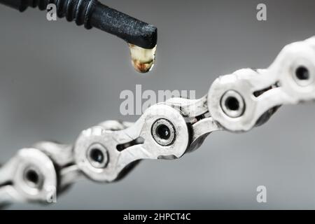 Schmieren einer Fahrradkette mit einem Tropfen goldenem Öl aus nächster Nähe auf grauem Hintergrund. Pflege des Fahrradantriebs. Stockfoto