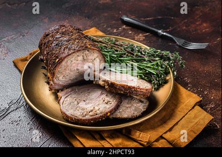 Scheiben gebratene gefüllte Schweinefleischroulade auf einem Teller mit Rosmarin und Thymian. Dunkler Hintergrund. Draufsicht Stockfoto