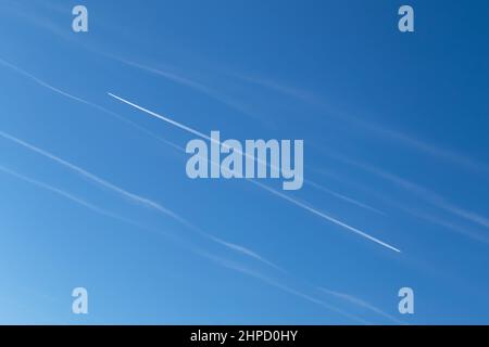 Contrails - zwei Flugzeuge fliegen in entgegengesetzte Richtungen mit weißen Kondensstreifen am blauen Himmel Stockfoto