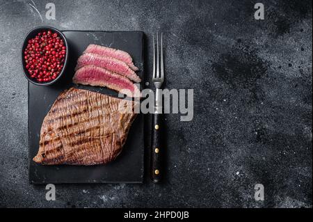 Gegrilltes Flanke Steak BBQ auf einem Marmorbrett. Schwarzer Hintergrund. Draufsicht. Speicherplatz kopieren Stockfoto