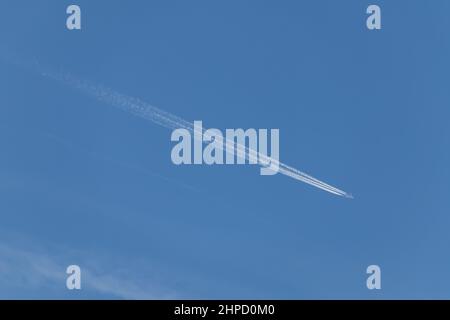 Contrails - ein fliegendes Transportflugzeug mit weißen Kondensstreifen am blauen Himmel Stockfoto