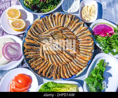 Ein Teller mit frittierten knusprigen Sardellen, türkischer Name Hamsı Tava in Maismehl mit Zitrone, verschiedenen Grüns und Vorspeisen, traditionelle türkische Küche. Stockfoto