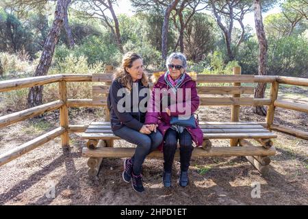 Eine reife Frau hält die Hand ihrer älteren Mutter, während sie auf einer Bank sitzt Stockfoto