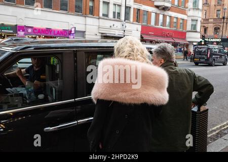 Ein älteres Paar hagelt ein Londoner Taxi auf der Charing Cross Road, London, Großbritannien Stockfoto