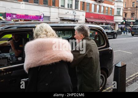 Ein älteres Paar hagelt ein Londoner Taxi auf der Charing Cross Road, London, Großbritannien Stockfoto