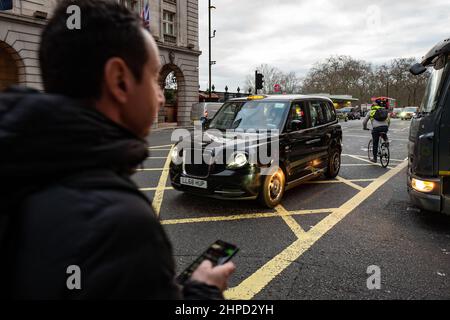 Das schwarze Londoner Taxi fährt an der geschäftigen Oxford Street in eine gelbe Kreuzung ein. Stockfoto