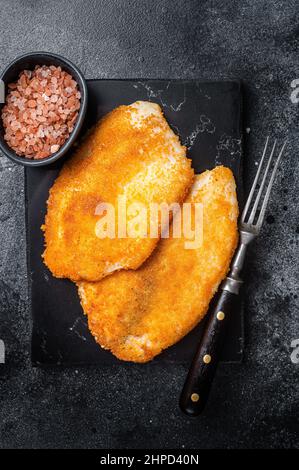 Gebratene panierte Tilapia-Filets auf einem Marmorbrett. Schwarzer Hintergrund. Draufsicht Stockfoto