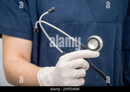 Arzt in medizinischen Uniform hält, in der Hand mit Einweghandschuh, Stethoskop, das aus Disk-förmigen Resonator und Schlauch mit Ohrstück besteht. Gesundheitswesen Stockfoto