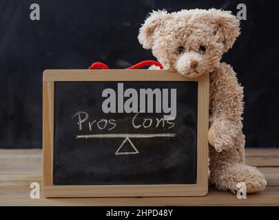 Pros contra contra Konzept. Teddybär auf Holztisch mit gerahmter Tafel mit leerer Liste auf Tafel-Hintergrund, zur Analyse und Entscheidung Stockfoto